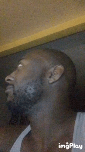 A Man With A Beard Is Wearing A White Tank Top And Looking Up .. GIF