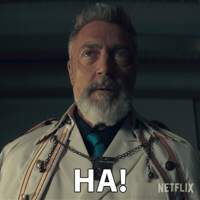 A Man With A Beard Is Wearing A White Trench Coat And A Necklace With The Word Ha On It GIF