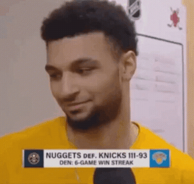 A Man With A Beard Is Wearing A Yellow Shirt And Talking Into A Microphone In A Locker Room . GIF