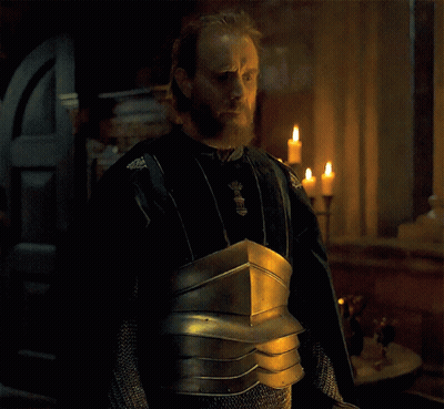A Man With A Beard Is Wearing Armor And Standing In Front Of A Window With Candles GIF