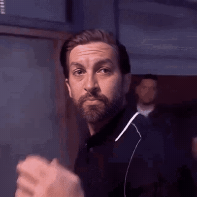 A Man With A Beard Is Wearing Ear Buds And Making A Funny Face . GIF
