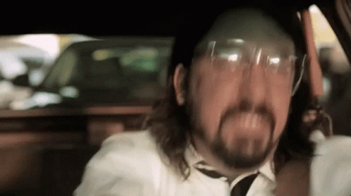 A Man With A Beard Is Wearing Glasses And A Tie While Driving A Car . GIF