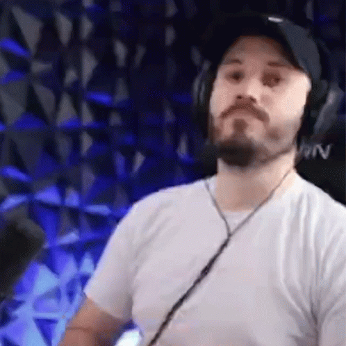 A Man With A Beard Is Wearing Headphones And A Hat In Front Of A Microphone . GIF