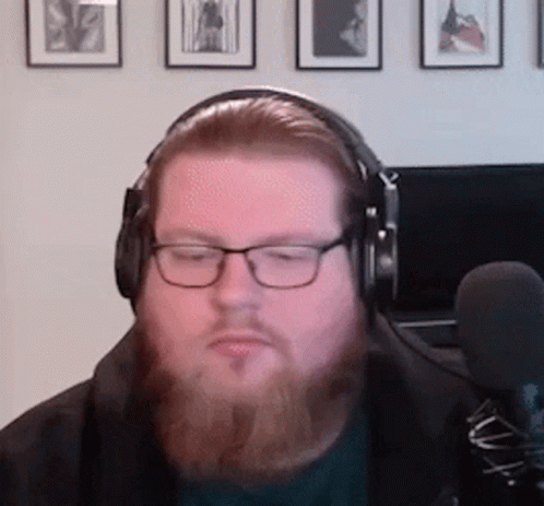 A Man With A Beard Is Wearing Headphones And Glasses While Sitting In Front Of A Microphone . GIF