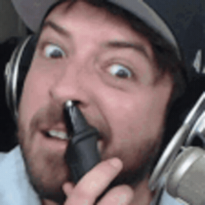 A Man With A Beard Is Wearing Headphones And Holding A Microphone In His Hand . GIF