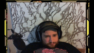 A Man With A Beard Is Wearing Headphones And Holding A Microphone While Sitting On A Bed GIF