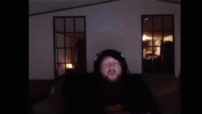 A Man With A Beard Is Wearing Headphones And Making A Funny Face While Sitting In Front Of A Window . GIF