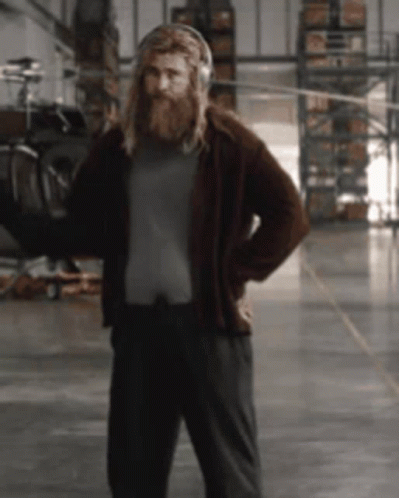 A Man With A Beard Is Wearing Headphones And Standing In A Warehouse GIF