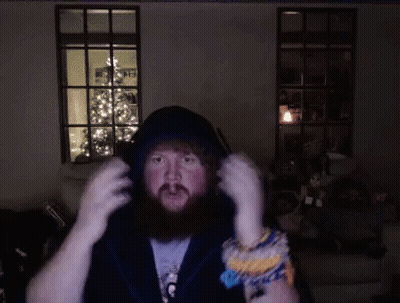 A Man With A Beard Is Wearing Headphones In A Dark Room With A Christmas Tree In The Background GIF