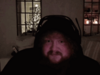 A Man With A Beard Is Wearing Headphones In A Dark Room With A Christmas Tree In The Background GIF