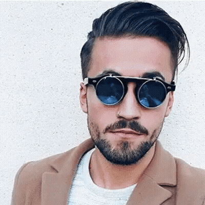 A Man With A Beard Is Wearing Sunglasses And A Coat . GIF
