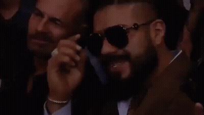 A Man With A Beard Is Wearing Sunglasses While Sitting In A Crowd Of People . GIF
