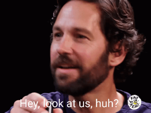A Man With A Beard Says Hey Look At Us Huh In Front Of A Black Background GIF