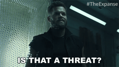 A Man With A Beard Says " Is That A Threat " In A Dark Room GIF