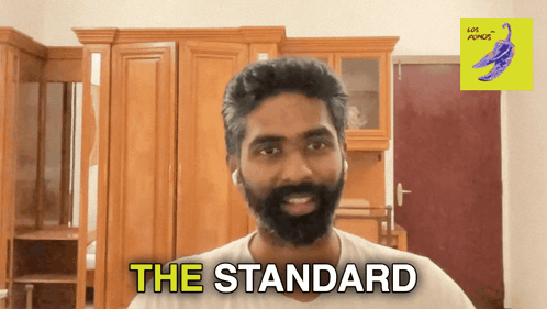 A Man With A Beard Says " The Standard " In A Room GIF