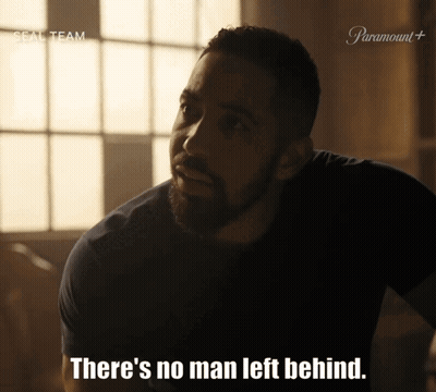 A Man With A Beard Says " There 'S No Man Left Behind " In A Dark Room GIF