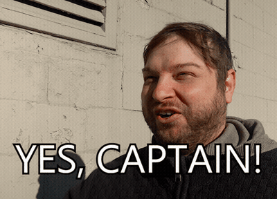 A Man With A Beard Says " Yes Captain " In Front Of A Brick Wall GIF