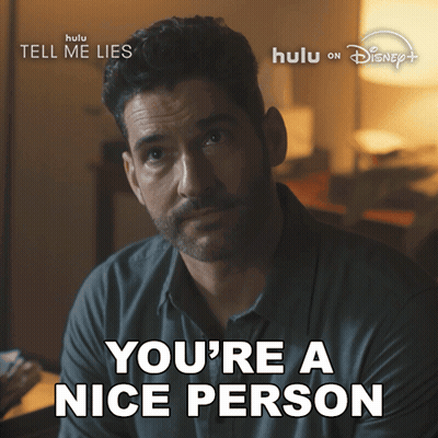A Man With A Beard Says " You 'Re A Nice Person " In Front Of A Poster For Tell Me Lies GIF