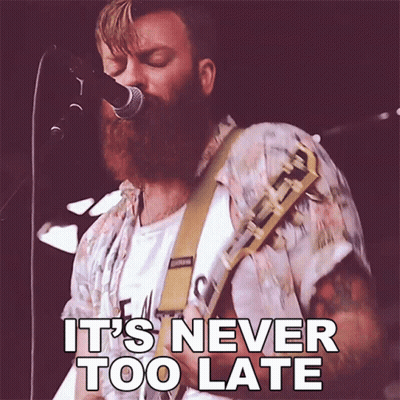 A Man With A Beard Singing Into A Microphone With The Words It 'S Never Too Late Below Him GIF
