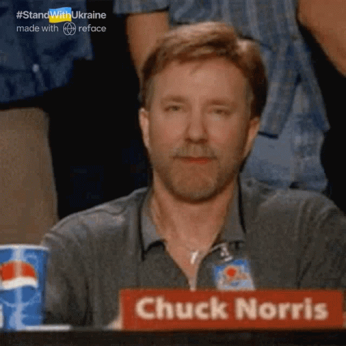 A Man With A Beard Sits At A Table With A Sign That Says Chuck Norris GIF