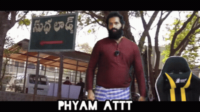 A Man With A Beard Standing In Front Of A Sign That Says Phyam Attt GIF