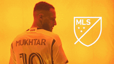 A Man With A Beard Stands In Front Of A Logo For The Mls GIF