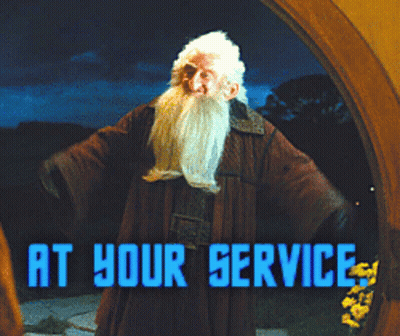 A Man With A Beard Stands In Front Of A Sign That Reads At Your Service GIF