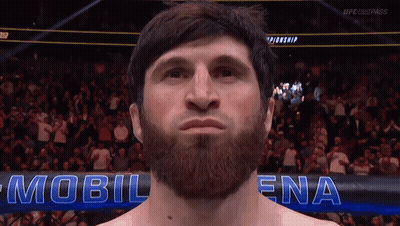 A Man With A Beard Stands In Front Of A Sign That Says Mobil Ena GIF