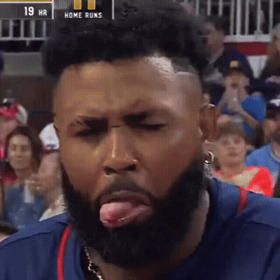A Man With A Beard Sticking His Tongue Out In Front Of A Scoreboard That Says Home Runs GIF