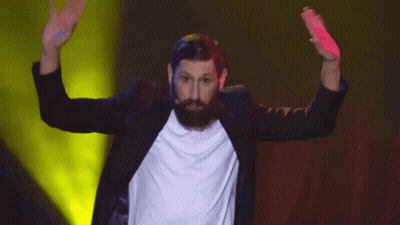 A Man With A Beard Wearing A Black Jacket And A White Shirt Is Dancing On A Stage GIF