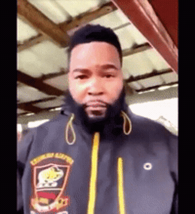 A Man With A Beard Wearing A Black Jacket With A Yellow Zipper GIF