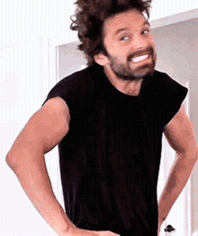 A Man With A Beard Wearing A Black Shirt Is Standing With His Hands On His Hips And Smiling . GIF