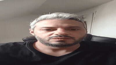 A Man With A Beard Wearing A Black Shirt Looks Down At The Camera GIF