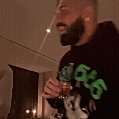 A Man With A Beard Wearing A Black Sweatshirt With Green Letters That Says 99 On It GIF