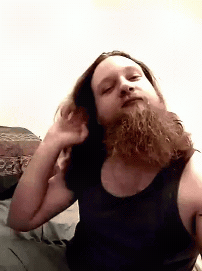 A Man With A Beard Wearing A Black Tank Top Looks At The Camera GIF