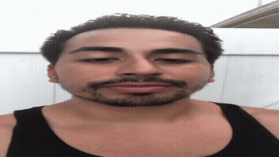 A Man With A Beard Wearing A Black Tank Top Looks At The Camera GIF
