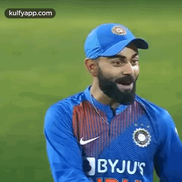 A Man With A Beard Wearing A Blue Hat And A Blue Shirt Is Standing On A Field . GIF