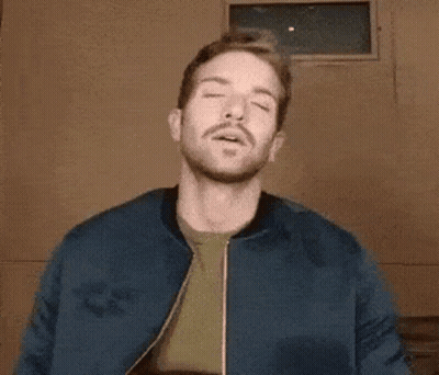 A Man With A Beard Wearing A Blue Jacket And A Green Shirt Is Making A Funny Face . GIF