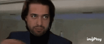 A Man With A Beard Wearing A Blue Suit And Black Turtleneck Is Looking Up . GIF