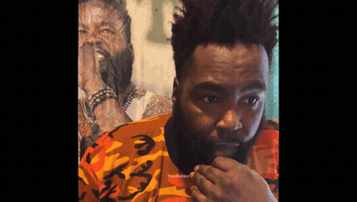 A Man With A Beard Wearing A Camouflage Shirt Looks At The Camera GIF