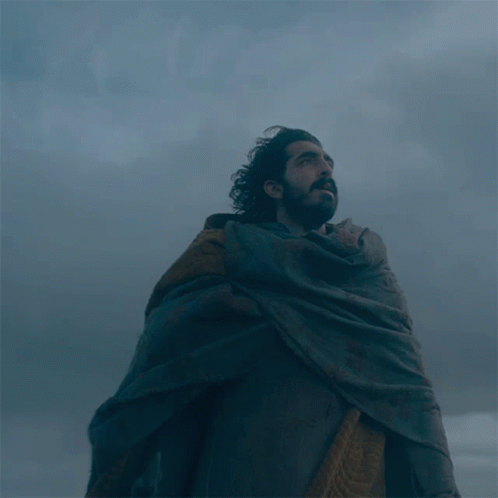 A Man With A Beard Wearing A Cape Looks Up Into The Sky GIF