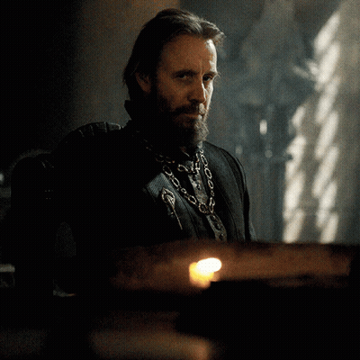A Man With A Beard Wearing A Chain Around His Neck Looks At The Camera GIF