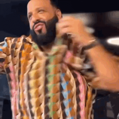 A Man With A Beard Wearing A Colorful Shirt Is Holding A Microphone . GIF