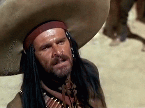 A Man With A Beard Wearing A Cowboy Hat And A Necklace Of Bullets GIF