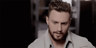 A Man With A Beard Wearing A Denim Shirt Looks At The Camera GIF
