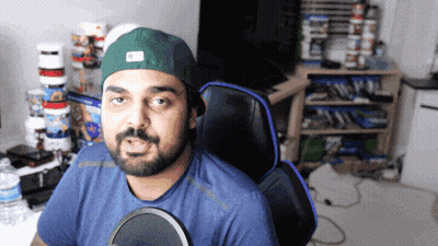 A Man With A Beard Wearing A Green Hat Is Sitting In A Chair GIF