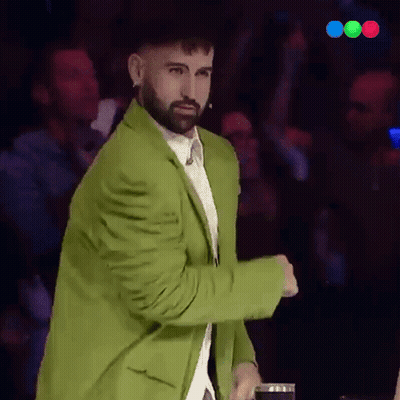 A Man With A Beard Wearing A Green Jacket Stands In Front Of A Crowd GIF
