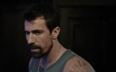 A Man With A Beard Wearing A Green Tank Top Looks At The Camera GIF