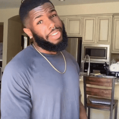 A Man With A Beard Wearing A Grey Shirt And A Gold Chain GIF