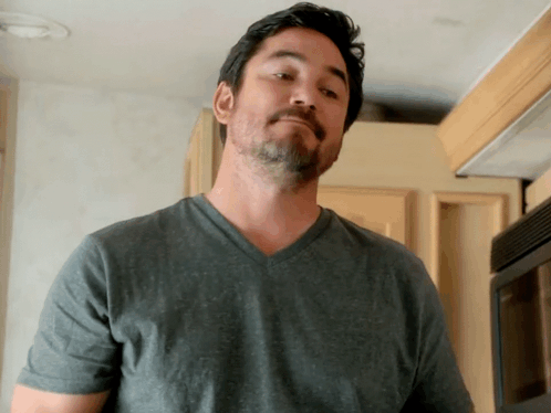 A Man With A Beard Wearing A Grey Shirt Looks At The Camera GIF
